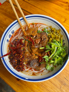 Bowl of round rice noodles with beef and greens
